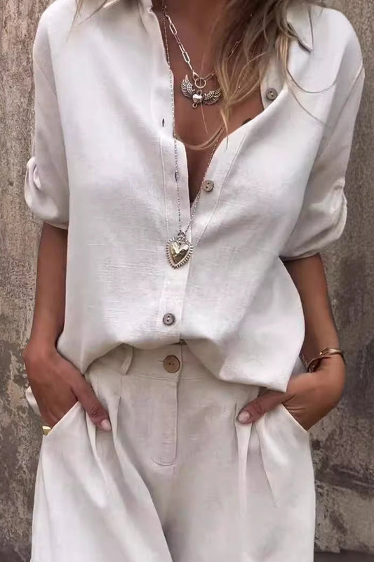 Frau in weißem Leinenhemd und Hose, trägt Herzanhänger und Ketten. Sommermode, lässiger Stil, elegante Damenbekleidung.