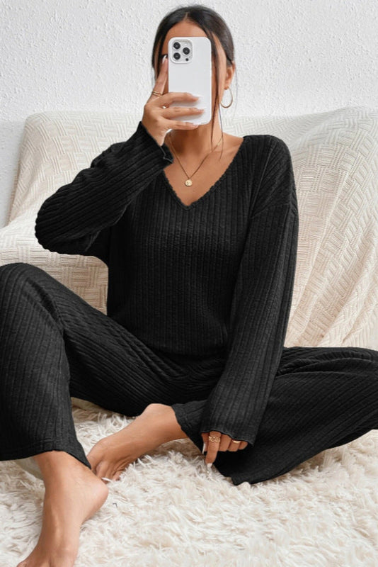 Frau in schwarzem Strick-Pyjama sitzt auf Sofa, hält Smartphone. Bequemes Lounge-Outfit, modernes Design, gemütliche Heimkleidung.