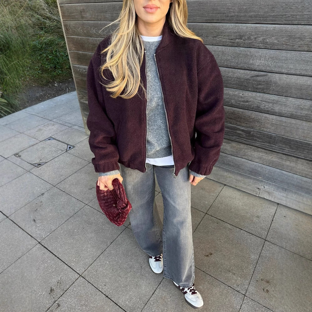 Frau in lässiger Herbstmode mit bordeauxroter Jacke, grauem Pullover, grauer Jeans und weißen Sneakers. Streetstyle, Mode, Damenbekleidung.