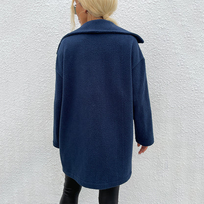 Frau in dunkelblauem Teddy-Mantel, Rückansicht, vor weißer Wand. Modetrend, Winterjacke, Damenbekleidung, stilvoll, warm, elegant.