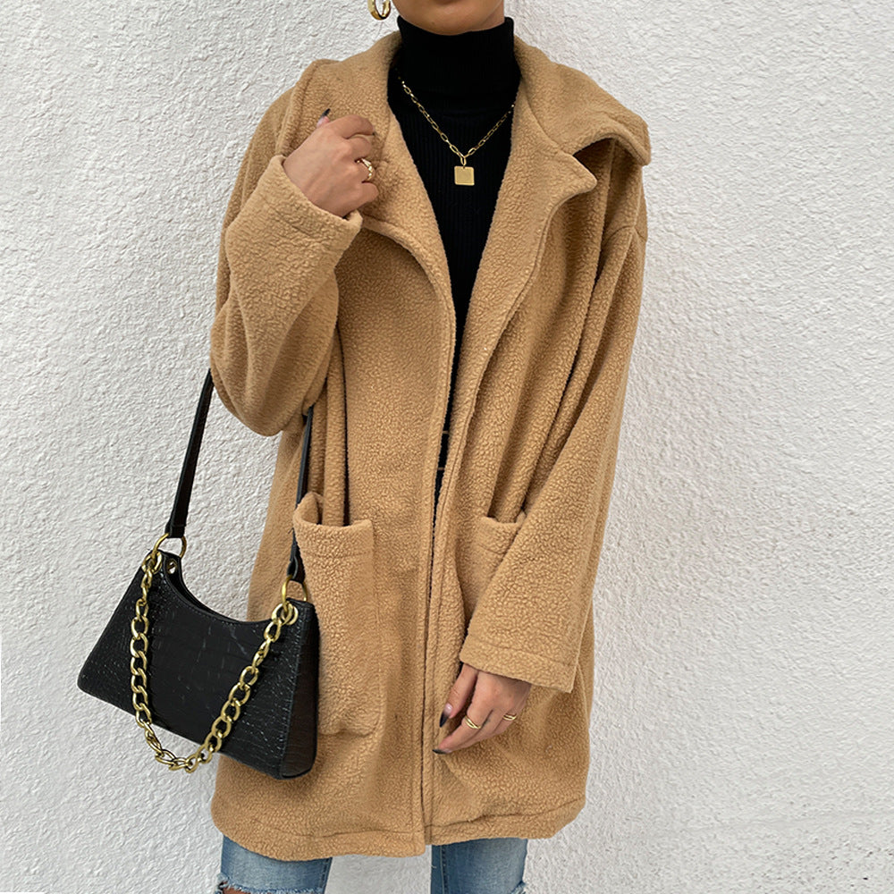 Dame in beigem Teddy-Mantel, schwarzem Rollkragenpullover und Jeans, trägt schwarze Handtasche mit goldener Kette. Wintermode, stilvoll, modern.