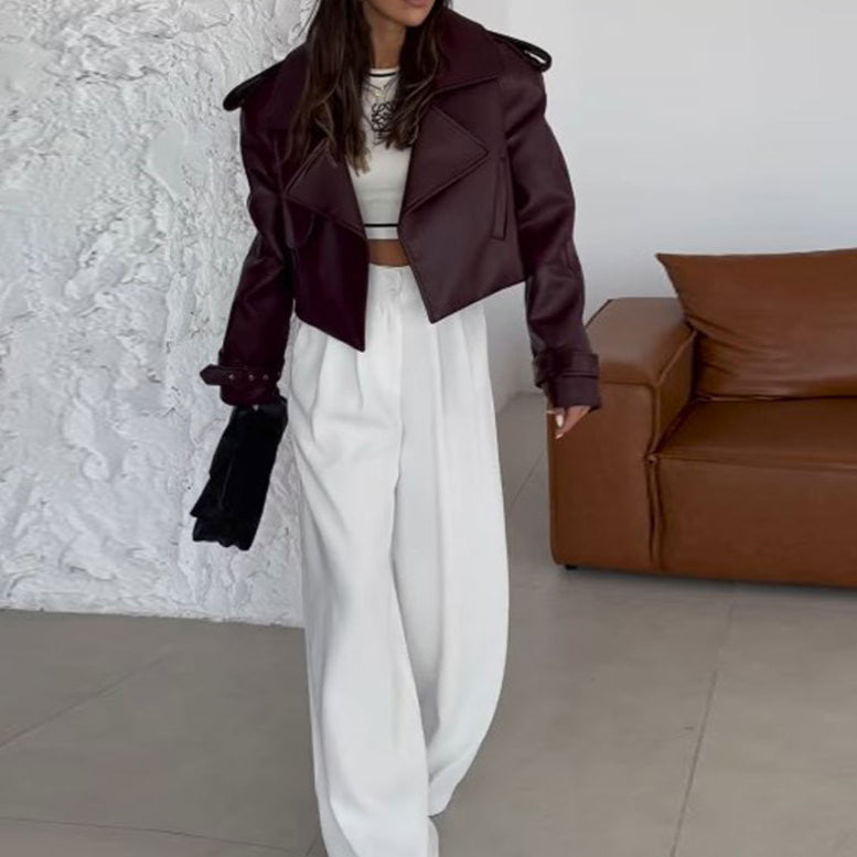 Frau in bordeauxroter Lederjacke und weißer Hose, hält schwarze Tasche. Moderne Mode, eleganter Look, stilvolle Damenbekleidung.