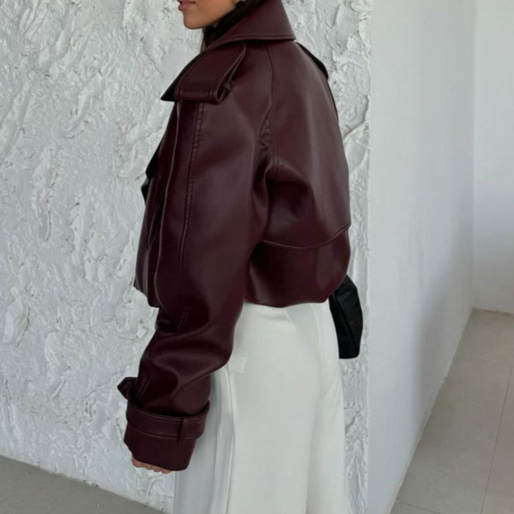 Frau in bordeauxroter Lederjacke und weißer Hose vor weißer Wand. Modetrend, Herbstmode, stilvolle Damenbekleidung.