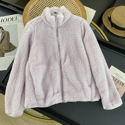 Fliederfarbene Fleecejacke auf einem Tisch, umgeben von Modezeitschriften und einem Strohhut. Weiche, kuschelige Textur, ideal für Herbstmode.