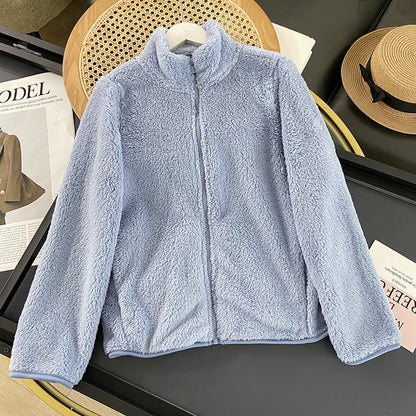 Hellblaue Fleecejacke auf Tisch, umgeben von Modezeitschriften und Strohhut. Weiche, kuschelige Textur, ideal für Herbstmode und Outdoor-Aktivitäten.