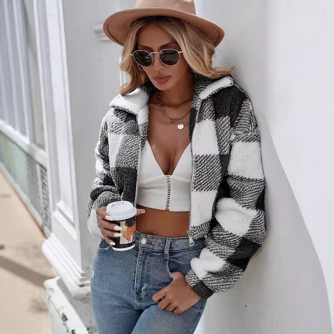 Frau in kariertem Mantel, weißem Top und Jeans, hält Kaffeebecher. Modetrend Herbst, stilvolle Sonnenbrille, brauner Hut, urbane Kulisse.