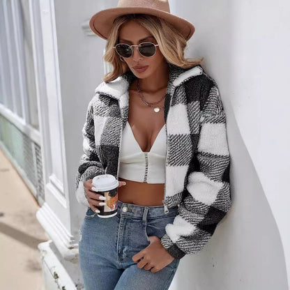 Frau in kariertem Mantel, weißem Top und Jeans, hält Kaffeebecher. Modetrend Herbst, stilvolle Sonnenbrille, brauner Hut, urbane Kulisse.