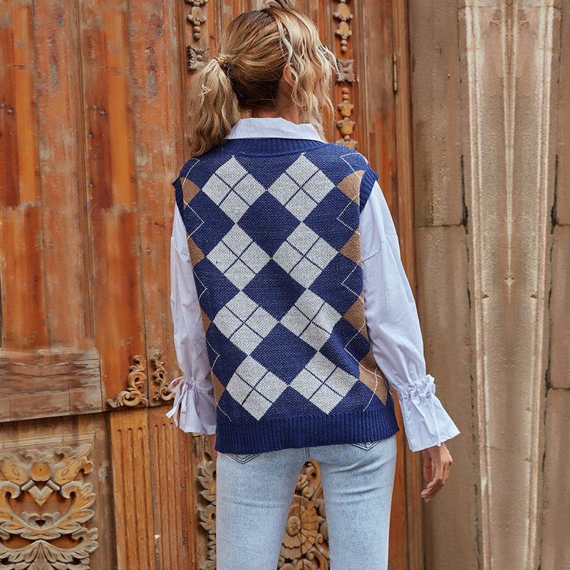 Frau mit blau-weißem Argyle-Pullover und weißer Bluse, steht vor antiker Holztür. Modetrend, Herbstmode, Damenbekleidung, Streetstyle.