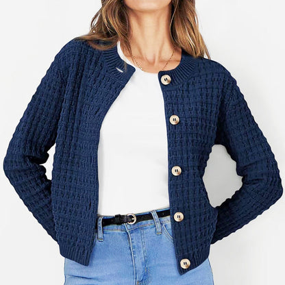 Frau trägt dunkelblauen Strick-Cardigan mit Knöpfen, kombiniert mit weißem T-Shirt und blauer Jeans. Modischer Damen-Look, Herbstmode.