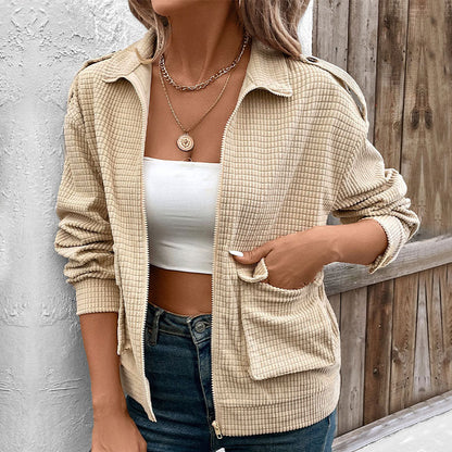 Frau in beiger Karo-Jacke, weißem Top und Jeans vor Holzwand. Modetrend, lässiger Stil, Damenmode, Herbstoutfit, Streetwear.