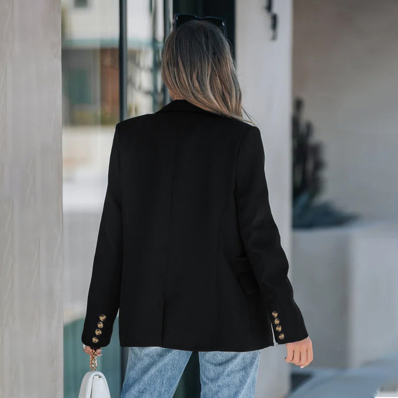 Frau in schwarzem Blazer mit goldenen Knöpfen und blauer Jeans, hält weiße Handtasche. Elegante Mode, Streetstyle, Rückansicht.
