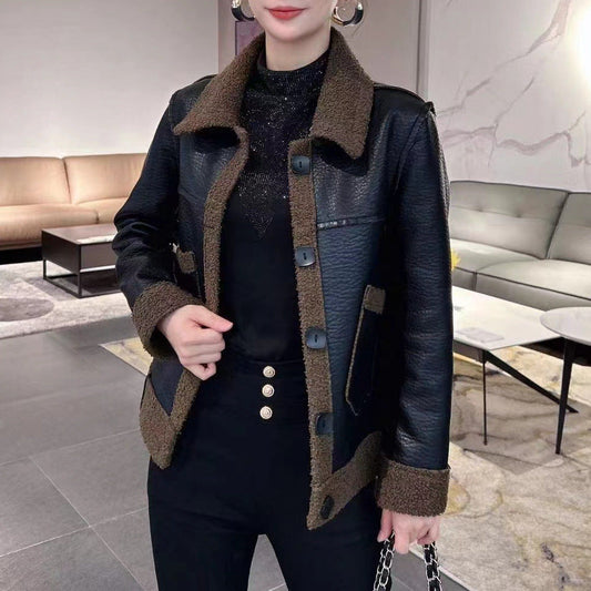 Frau in stilvoller schwarzer Lederjacke mit braunen Akzenten, eleganter schwarzer Hose und glitzerndem Oberteil in modernem Wohnzimmer.