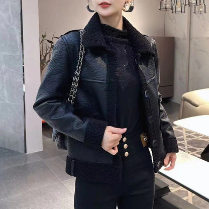 Frau in schwarzer Lederjacke mit Knöpfen, modisch gekleidet, steht in modernem Wohnzimmer. Stilvolle Damenmode, Herbst-Winter-Trend.