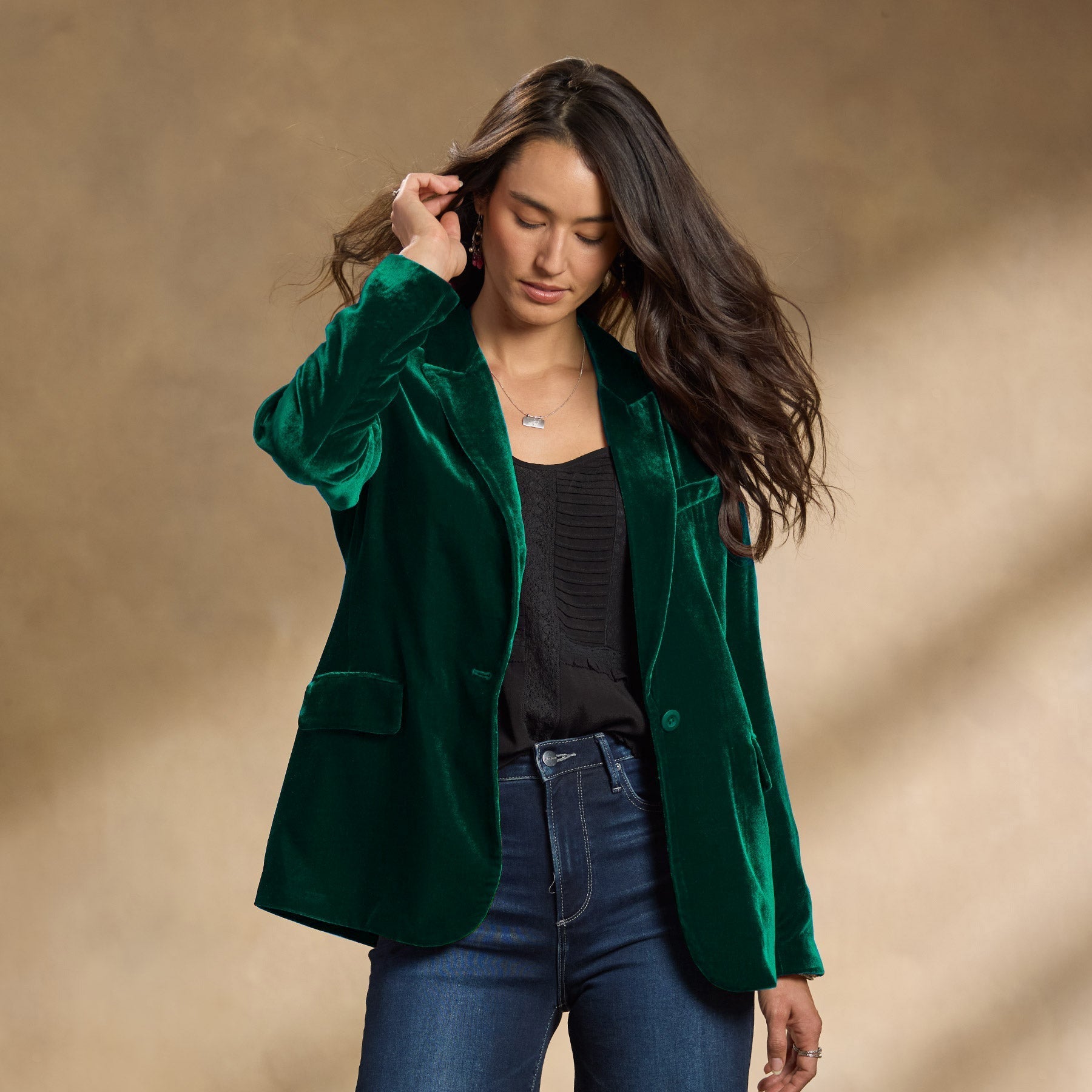 Frau in grünem Samtblazer, schwarzem Top und Jeans vor neutralem Hintergrund. Modetrend, eleganter Damenblazer, Herbstmode 2023.