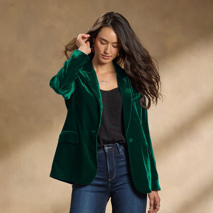 Frau in grünem Samtblazer, schwarzem Top und Jeans vor neutralem Hintergrund. Modetrend, eleganter Damenblazer, Herbstmode 2023.