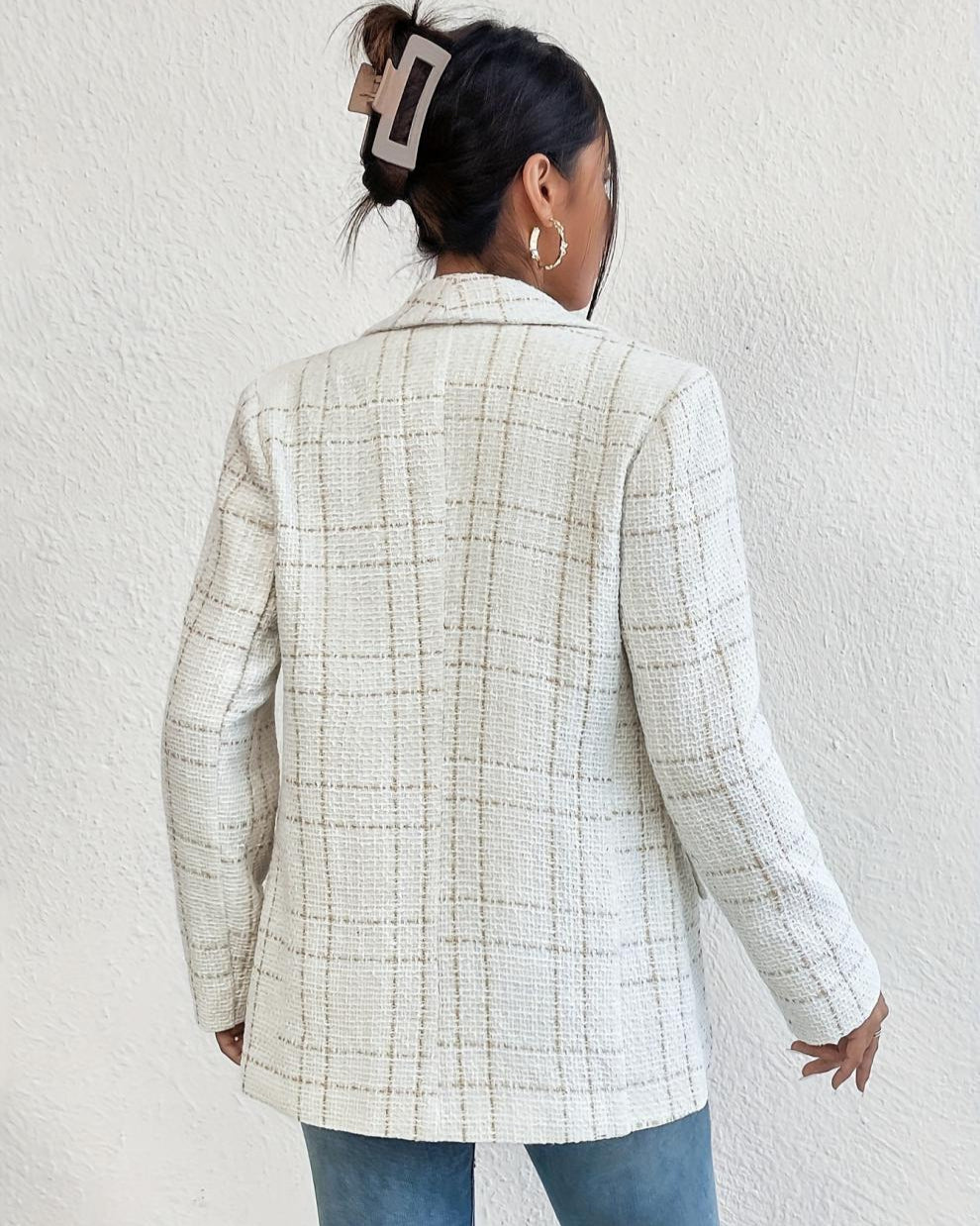 Frau mit weißem kariertem Blazer, Haarclip und goldenen Ohrringen, Rückansicht. Modetrend, eleganter Look, Damenmode, stilvoller Blazer.