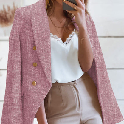 Frau in rosa Blazer mit goldenen Knöpfen, weißem Spitzen-Top und beigen Hosen, hält Smartphone. Elegante Damenmode, Business-Look.
