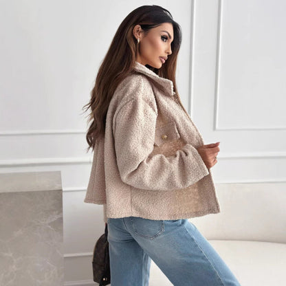 Frau in beiger Teddyjacke und blauer Jeans posiert seitlich in modernem, minimalistischem Raum. Modetrend, Herbstmode, Damenbekleidung.