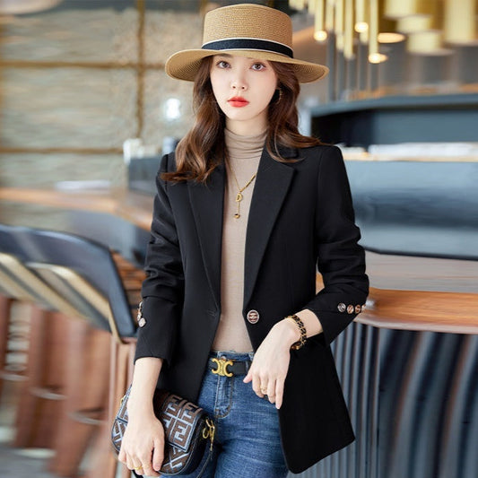 Frau in schwarzem Blazer und Strohhut, hält Designer-Handtasche, sitzt in modernem Café. Mode, Eleganz, Damenbekleidung, Accessoires.