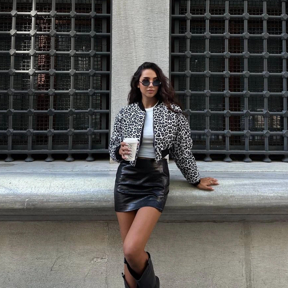 Frau in Leopardenjacke und Lederrock, hält Kaffeebecher, steht vor Gitterfenster. Modetrend, Streetstyle, urbane Mode, stilvolle Kleidung.