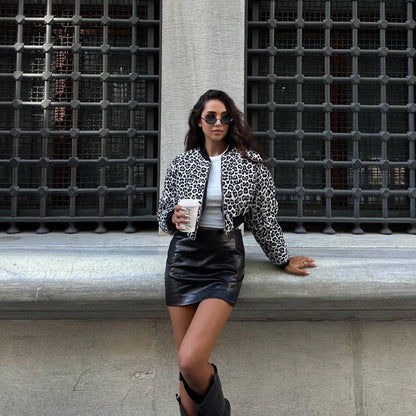 Frau in Leopardenjacke und Lederrock, hält Kaffeebecher, steht vor Gitterfenster. Modetrend, Streetstyle, urbane Mode, stilvolle Kleidung.