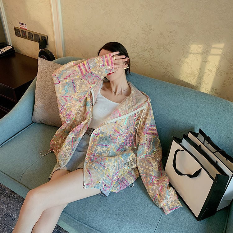 Frau auf Sofa mit bunter, glitzernder Jacke, hält Hand vor Gesicht. Neben ihr Einkaufstaschen. Moderne Mode, lässiger Stil, Innenraum.