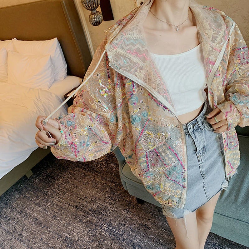 Frau in bestickter, transparenter Jacke mit bunten Mustern, weißem Top und Jeansrock im Schlafzimmer. Modetrend, Damenmode, stilvolle Kleidung.