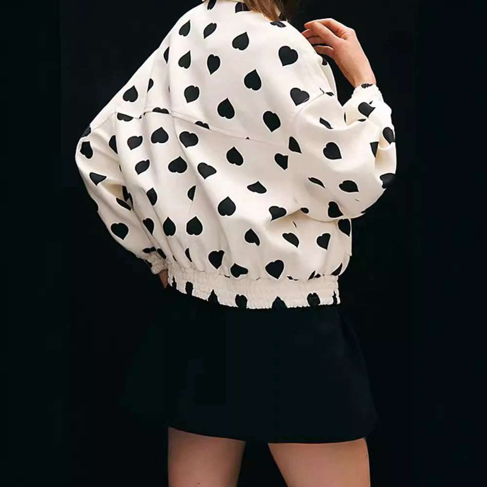 Weiße Jacke mit schwarzen Herzmustern, kombiniert mit schwarzem Rock. Modetrend, stilvolle Damenbekleidung, auffälliges Design.