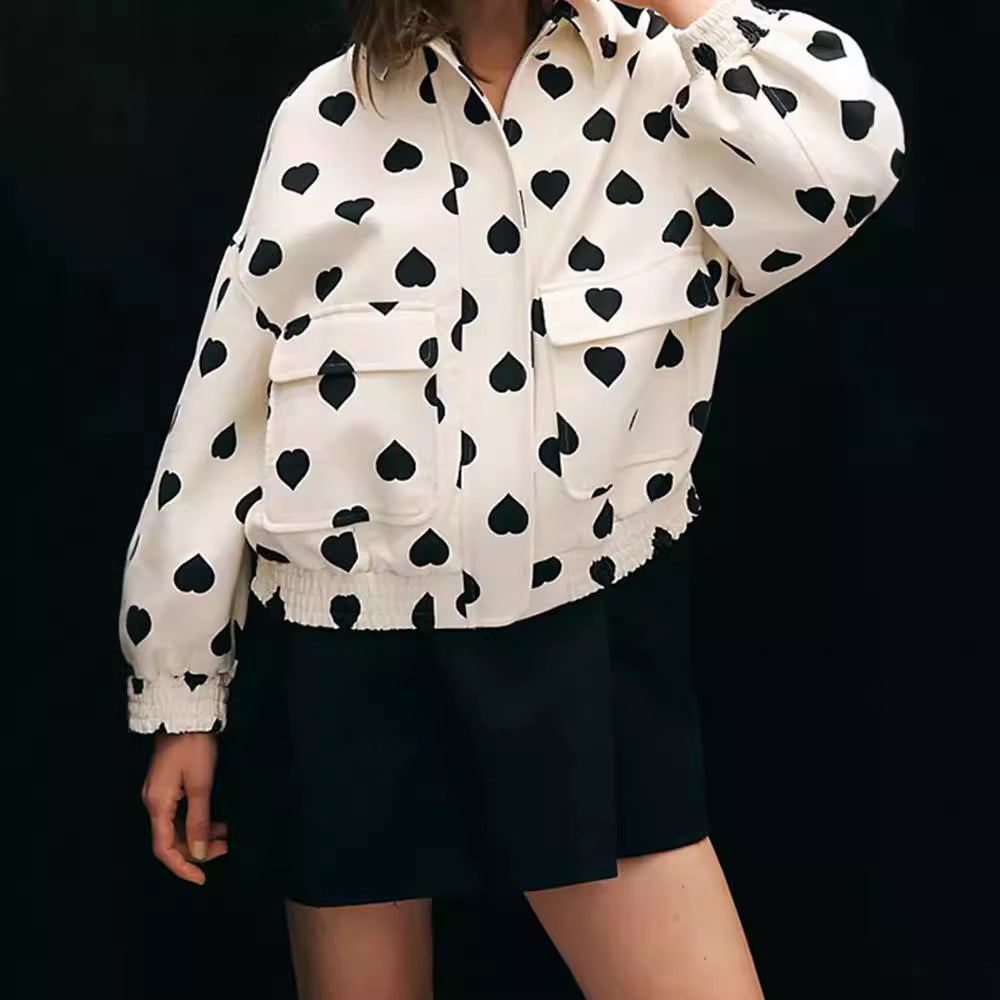 Frau trägt weiße Jacke mit schwarzen Herzmustern, kombiniert mit schwarzem Rock. Modetrend, stilvolle Damenbekleidung, Herzmuster-Jacke.