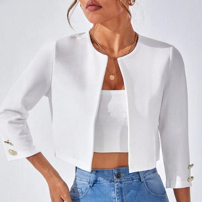 Weiße Damenjacke mit 3/4-Ärmeln, offenem Design und goldenen Knöpfen, kombiniert mit weißem Top und blauer Jeans. Elegante Mode für Frauen.