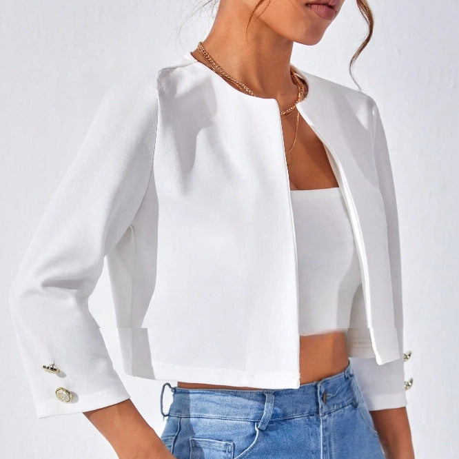 Weiße Damenjacke mit Dreiviertelärmeln und goldenen Knöpfen, kombiniert mit einem weißen Top und blauen Jeans. Elegante, moderne Damenmode.