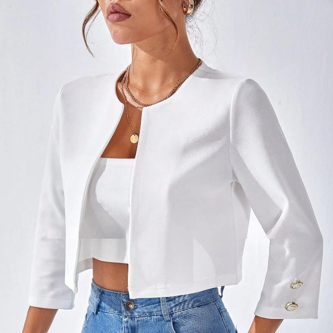 Weiße Damenjacke mit Dreiviertelärmeln und goldenen Knöpfen, kombiniert mit einem weißen Top und blauen Jeans. Elegante, moderne Damenmode.