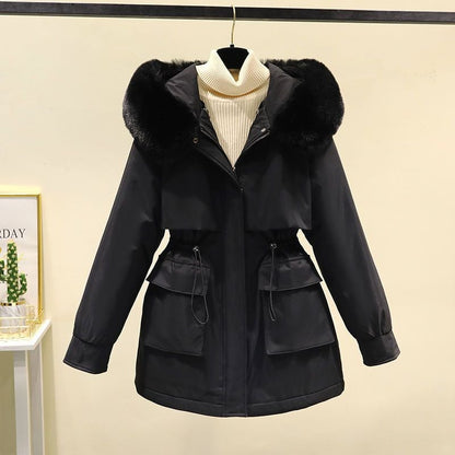 Schwarze Damenwinterjacke mit Kapuze und Kunstfellbesatz, Taillenzug, zwei Taschen, auf Kleiderbügel vor beigem Hintergrund.