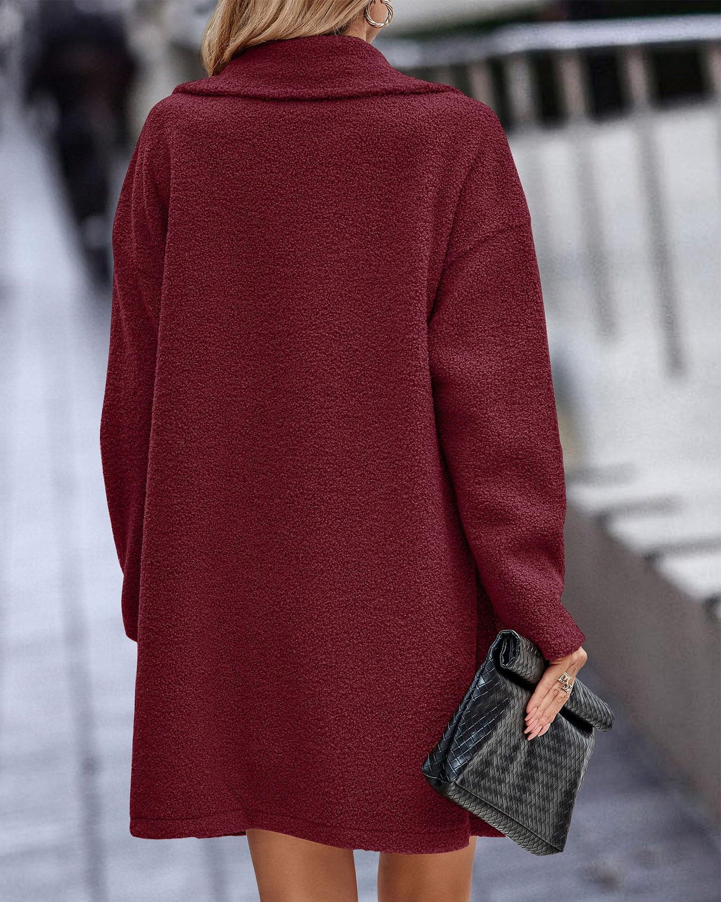 Frau in rotem Wollmantel von hinten, hält schwarze Clutch. Stilvolle Herbstmode, elegantes Outfit, urbane Kulisse.