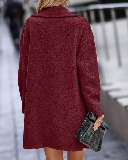 Frau in rotem Wollmantel von hinten, hält schwarze Clutch. Stilvolle Herbstmode, elegantes Outfit, urbane Kulisse.