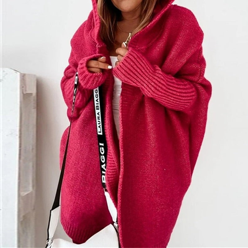 Frau in rotem Strick-Cardigan mit Kapuze, hält weiße Laura Biaggi Tasche. Modetrend, Herbstmode, gemütlicher Oversize-Look.