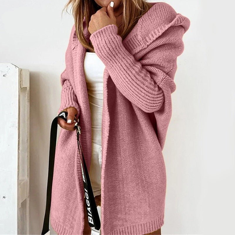 Frau in rosa Strickjacke mit Kapuze, weißem Top und Shorts. Modetrend, gemütlicher Herbstlook, Damenbekleidung, lässiger Stil.
