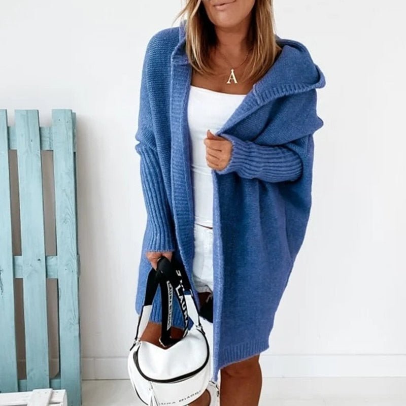 Frau in blauem Strick-Cardigan mit Kapuze, weißem Top und Shorts, hält weiße Handtasche. Modetrend, lässiger Herbstlook, Damenmode.