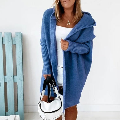 Frau in blauem Strick-Cardigan mit Kapuze, weißem Top und Shorts, hält weiße Handtasche. Modetrend, lässiger Herbstlook, Damenmode.