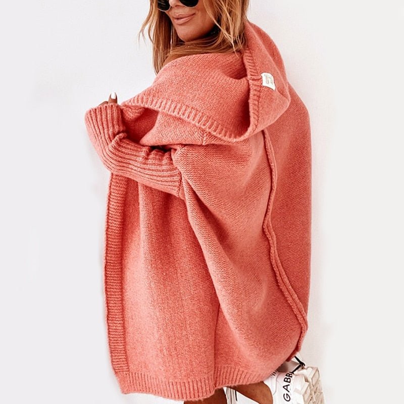 Frau in rosa Strickjacke mit Kapuze, lässiger Stil, trägt Sonnenbrille, weiße Sneakers. Modetrend Herbst, gemütliche Damenbekleidung.