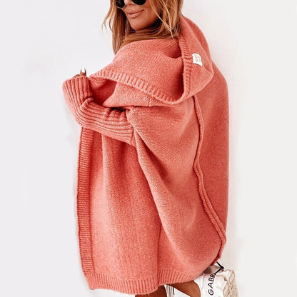 Frau in rosa Strickjacke mit Kapuze, lässiger Stil, trägt Sonnenbrille, weiße Sneakers. Modetrend Herbst, gemütliche Damenbekleidung.