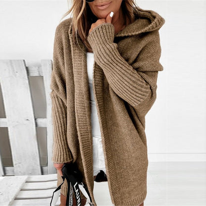 Frau in braunem Strick-Cardigan mit Kapuze, lässiger Herbstmode, hält schwarze Tasche. Trendige Damenbekleidung, gemütlicher Look.