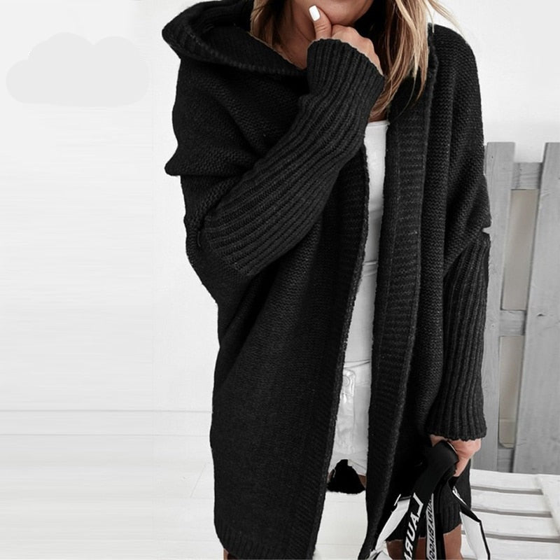 Frau in schwarzem Strick-Cardigan mit Kapuze, hält eine Tasche. Modischer Herbst-Look, gemütlicher Oversize-Stil, ideal für kühle Tage.