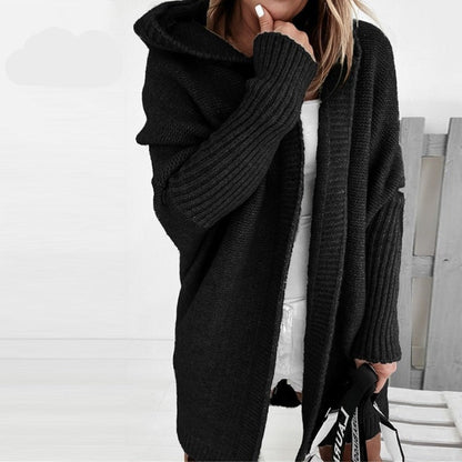 Frau in schwarzem Strick-Cardigan mit Kapuze, hält eine Tasche. Modischer Herbst-Look, gemütlicher Oversize-Stil, ideal für kühle Tage.