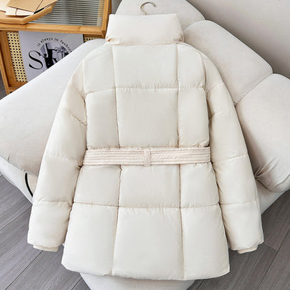 Weiße Daunenjacke mit Gürtel auf Sofa, modisch und warm, ideal für Wintermode. Hochwertige Steppjacke, stilvoll und bequem für kalte Tage.