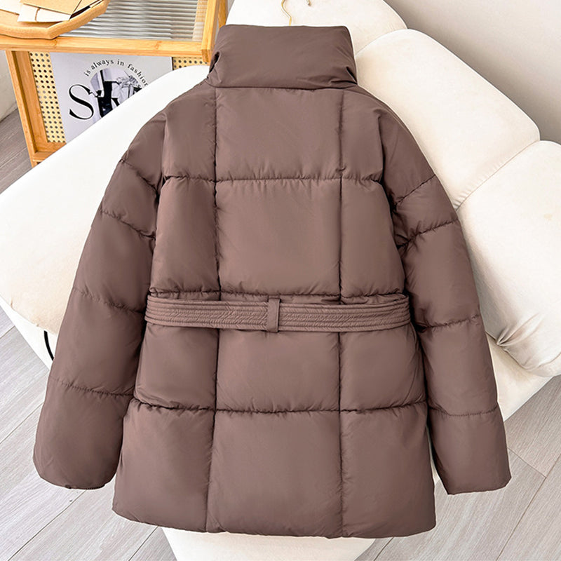 Braune Daunenjacke auf beigem Sofa, modisch und warm, ideal für Winterkleidung. Hochwertige Steppjacke mit Gürtel, stilvoll und funktional.