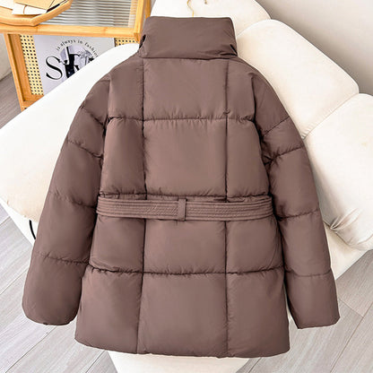 Braune Daunenjacke auf beigem Sofa, modisch und warm, ideal für Winterkleidung. Hochwertige Steppjacke mit Gürtel, stilvoll und funktional.