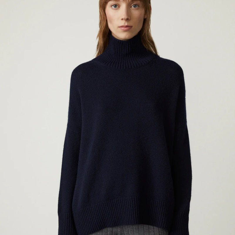 Frau in dunkelblauem Rollkragenpullover, minimalistisches Design, Herbstmode, gemütlicher Strick, stilvoller Look, neutrale Hintergrundfarbe.