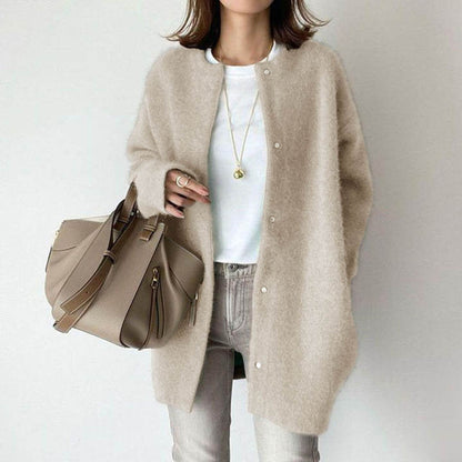 Frau in beigem Strickmantel, weißem T-Shirt und grauer Hose, hält eine beige Handtasche. Modetrend, Herbstmode, Damenbekleidung.