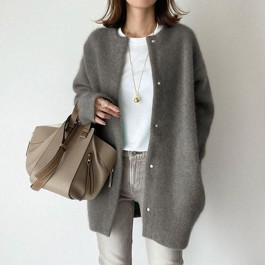 Frau in grauem Strickmantel, weißem T-Shirt und Jeans, hält beige Handtasche. Modischer Herbst-Look, lässig und elegant.